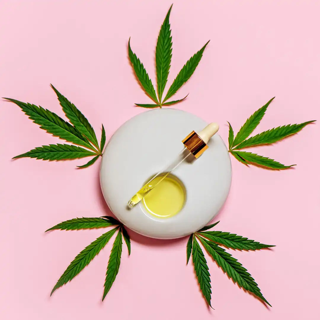 Bottle of CBD or cannabis oil surrounded by marijuana leaves on a white circular platform.