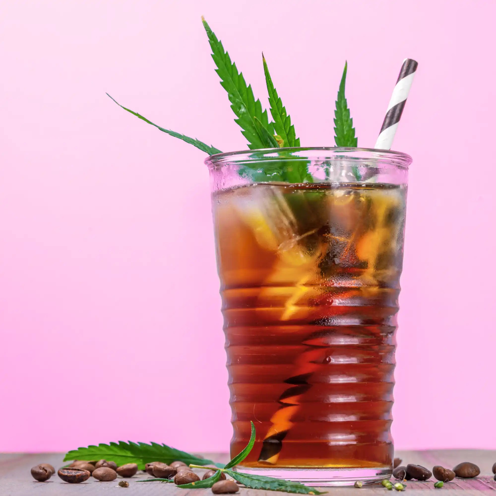 Glass of iced tea garnished with cannabis leaves and a striped straw.