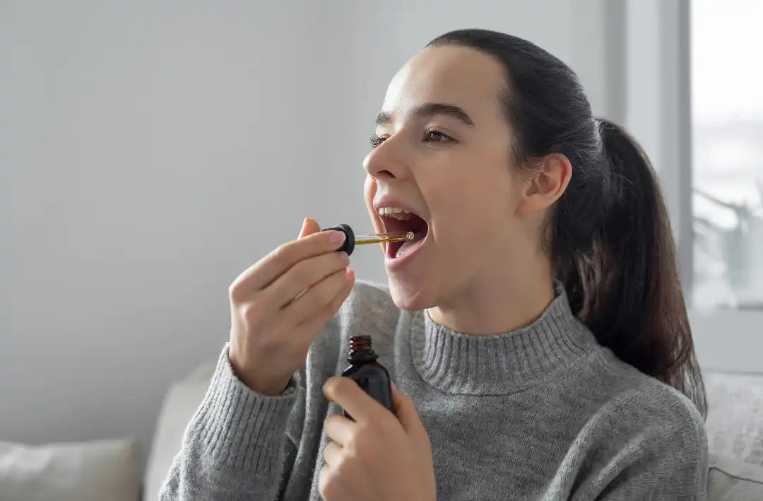 Woman with long dark hair wearing a gray sweater, singing or speaking into a microphone while holding a small object near her mouth.